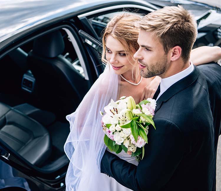 Handsome bridegroom in suit hugging attractive and blonde bride with bouquet