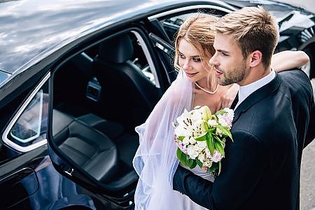 Handsome bridegroom in suit hugging attractive and blonde bride with bouquet